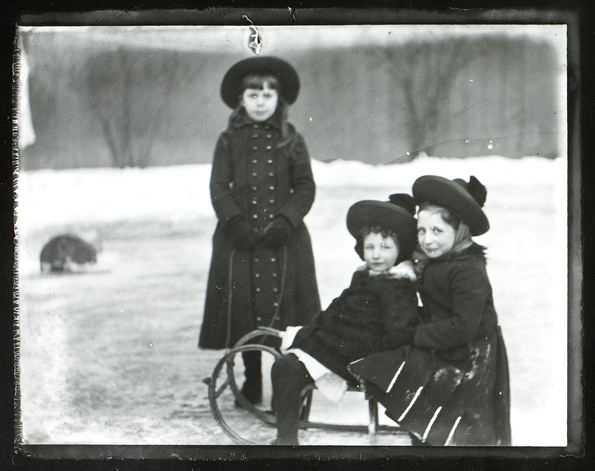 Two girls sit on a sled and one girl stands behind them