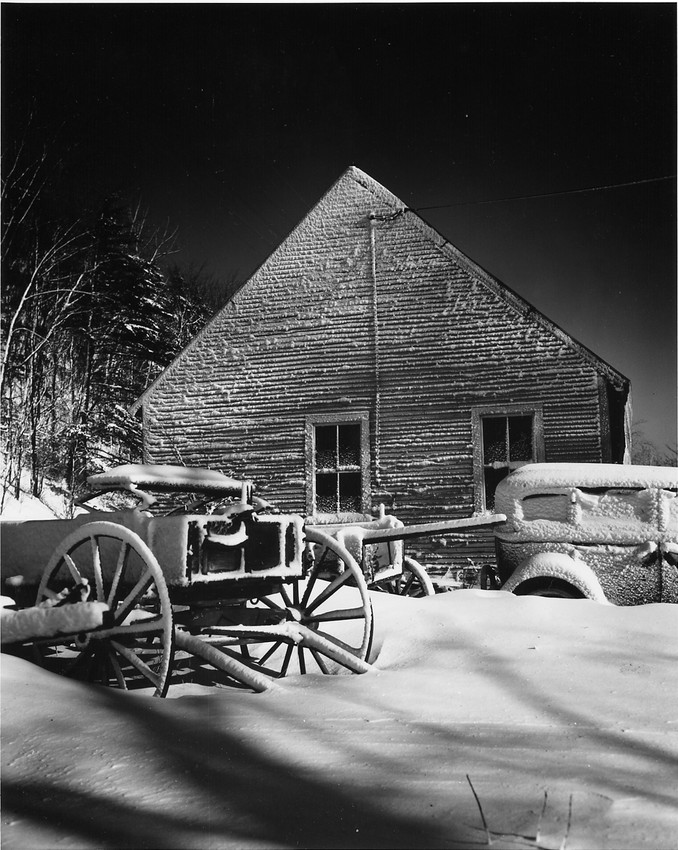 A buggy and a car sit under a blanket of snow next to a house