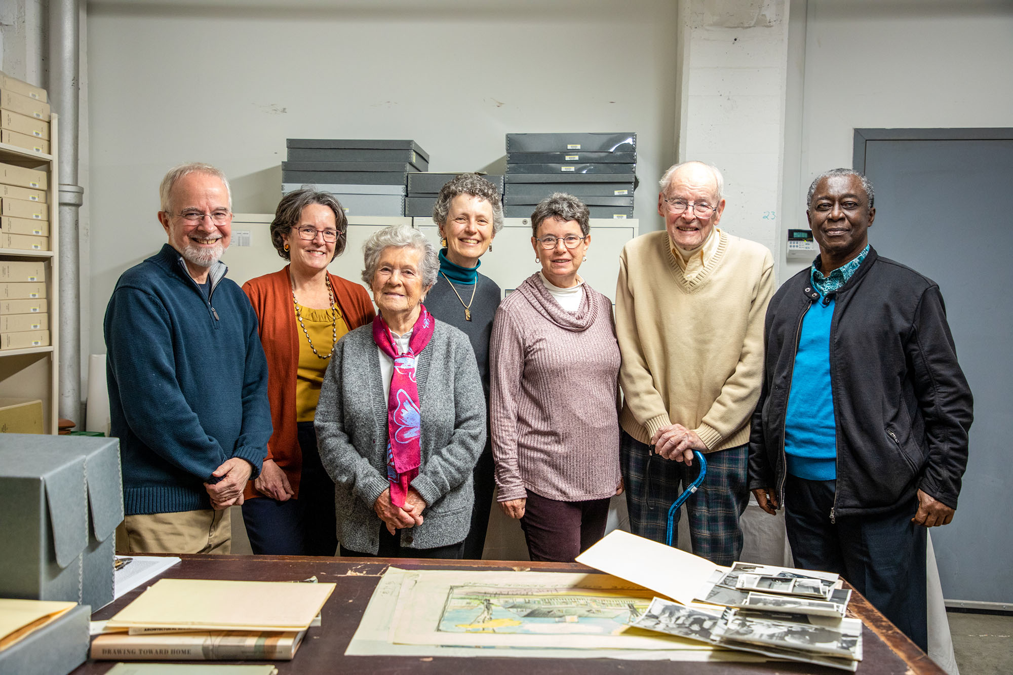 Seven of Royal Barry Wills's family members visiting the Library & Archives pose in front of a table with the architect's sketches.