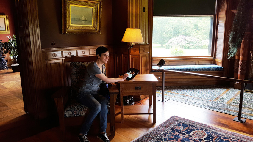 A visitor uses the Eustis Estate tour app while sitting in the large parlor
