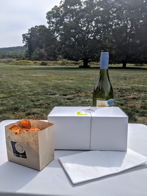 Bottle of wine and catered meal box on a table on the Eustis Estate lawn